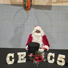 Santa figure sitting at a table with decorative letters and a hat.