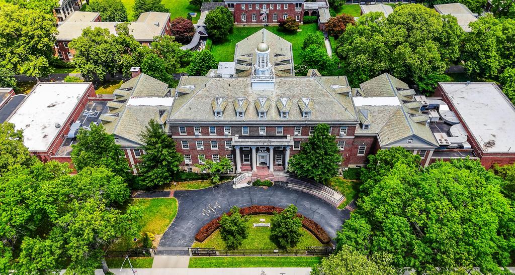 Aerial view of a large brick building surrounded by green trees and landscaping.
