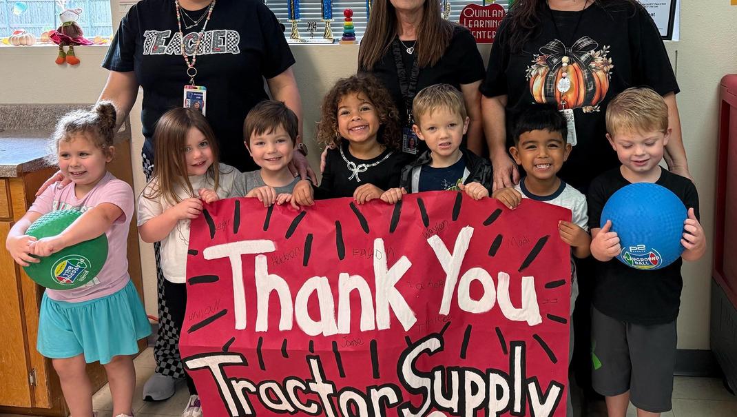 Group of children and adults holding a large thank you banner in a classroom.
