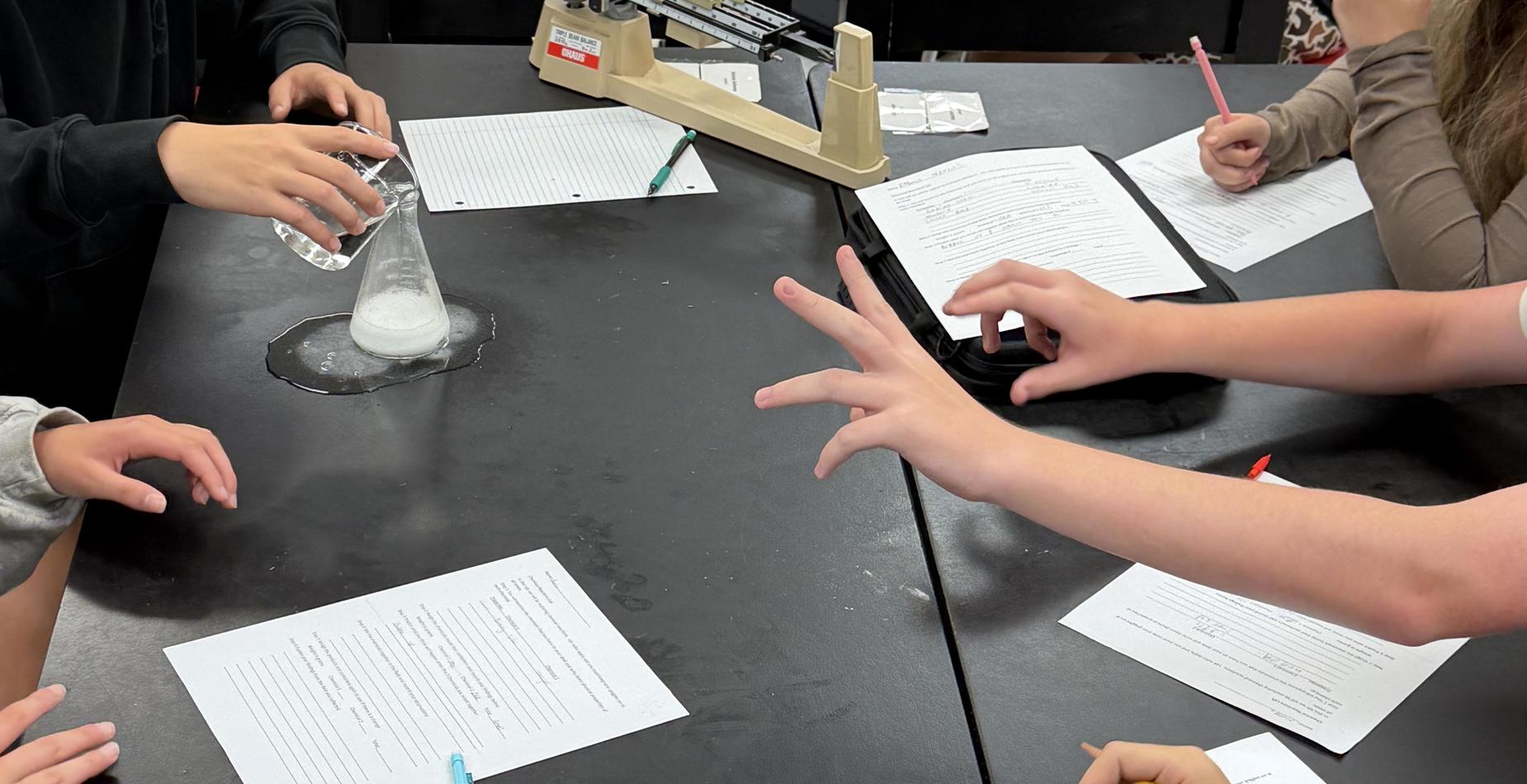 Students conducting a science experiment with papers and equipment on a table.