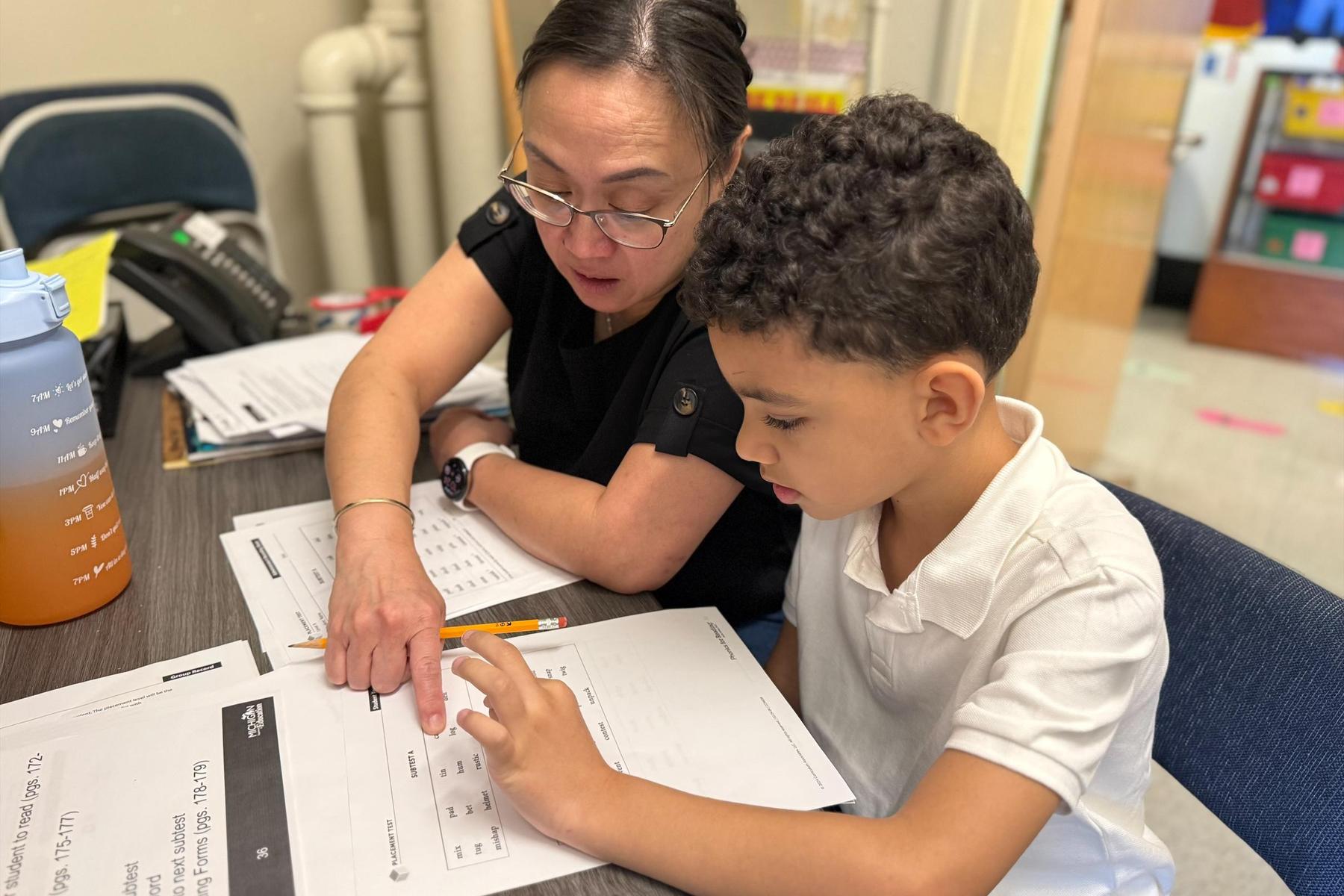 Teacher assisting a child with learning materials at a desk.