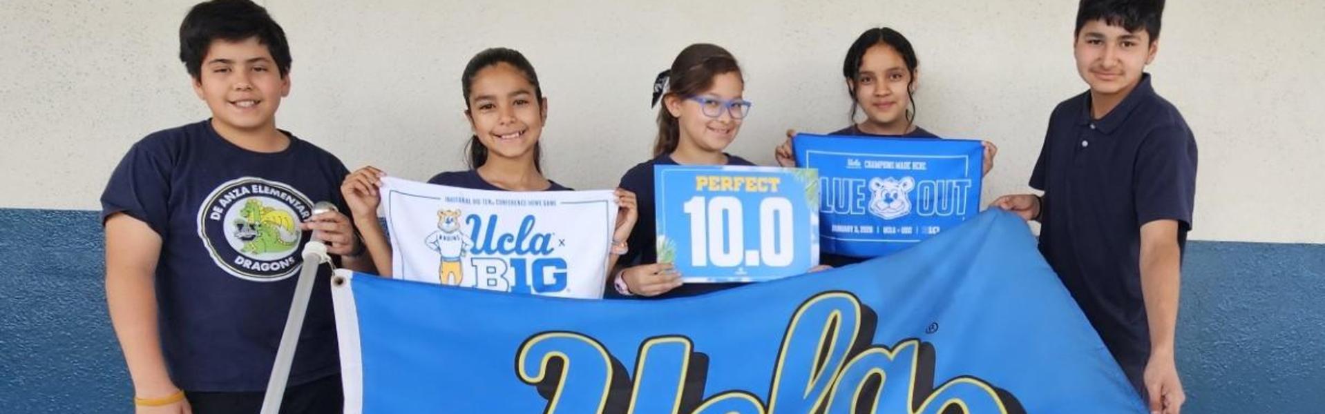 Group of students holding a UCLA flag and signs in a school setting.