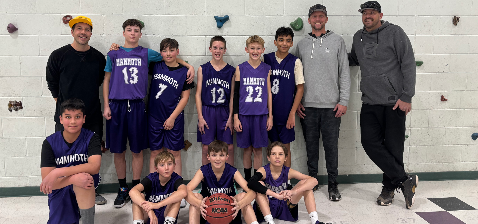 Group of young basketball players in uniforms with coaches, smiling in a gym.