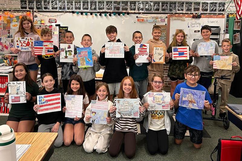 A large group of students smile and hold their drawings of flags
