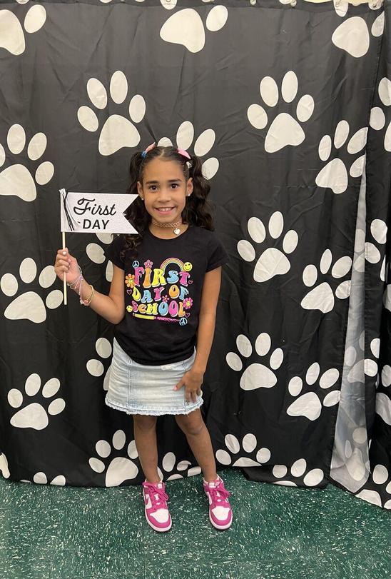A girl holding a firs day sign in front of a black and white paws backdrop1st day of school