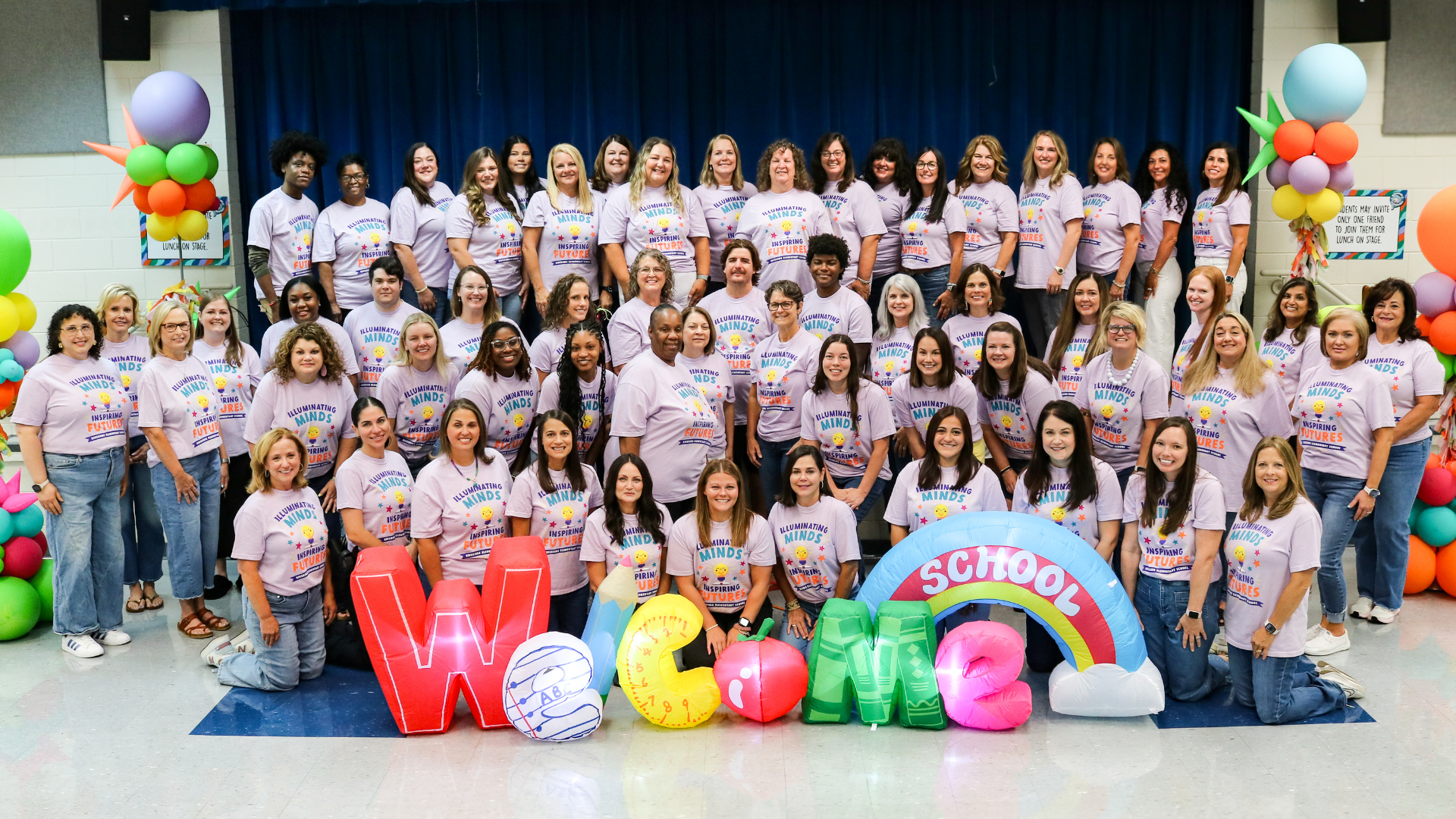 Group of educators in matching shirts with colorful decorations in a school setting.