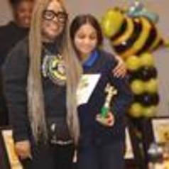 A woman and a girl pose together with a trophy, smiling at an event.