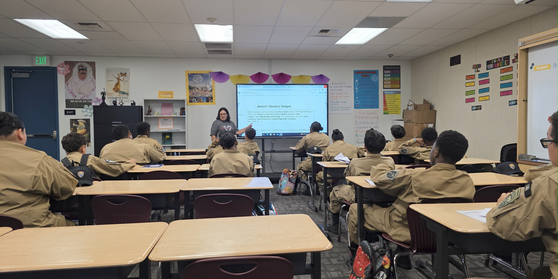 Classroom scene with a teacher presenting to students seated at desks.