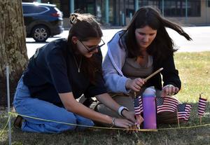 Two young women set up small flags on grass, focused on their task.