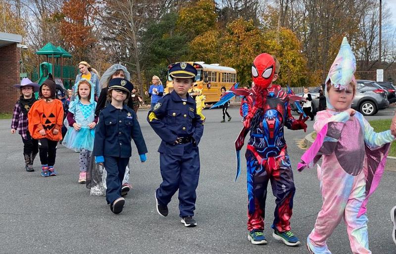Children in costumes, including superheroes and a police officer, walk together during a parade.