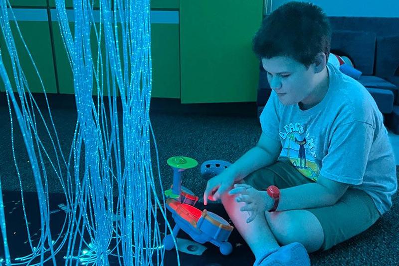 A student sits on the floor and is mesmerized by the hanging glow light and new toys to use while in the sensory room