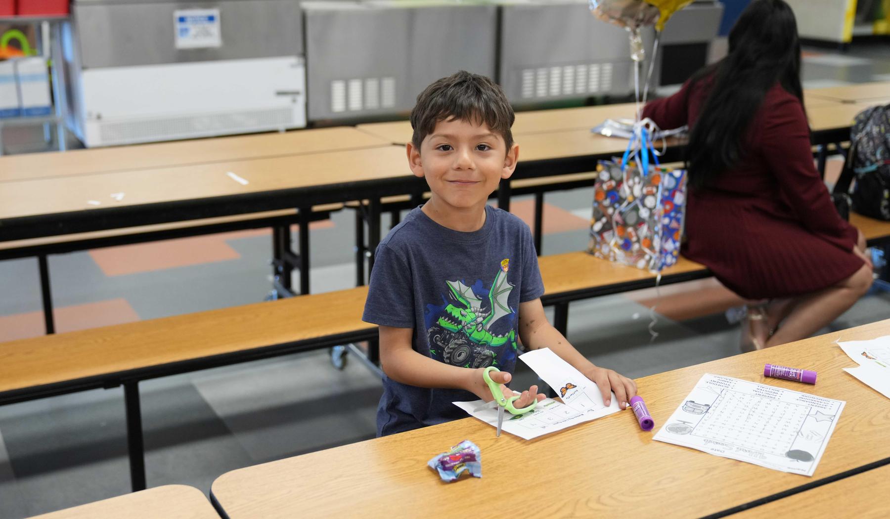 A young boy at a table, crafting with markers and paper in a school setting.