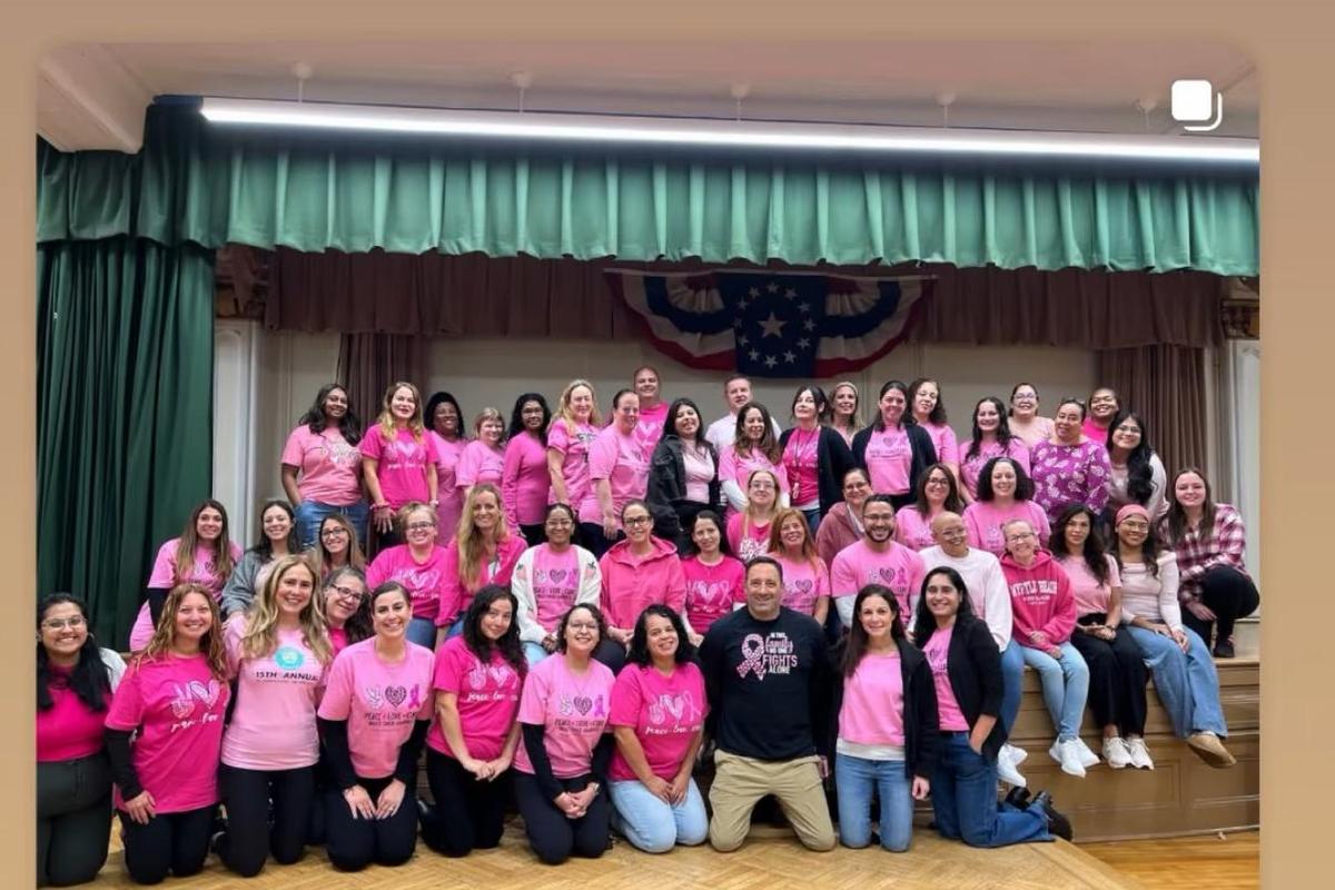 Large group of adults in pink shirts posing together on stage.