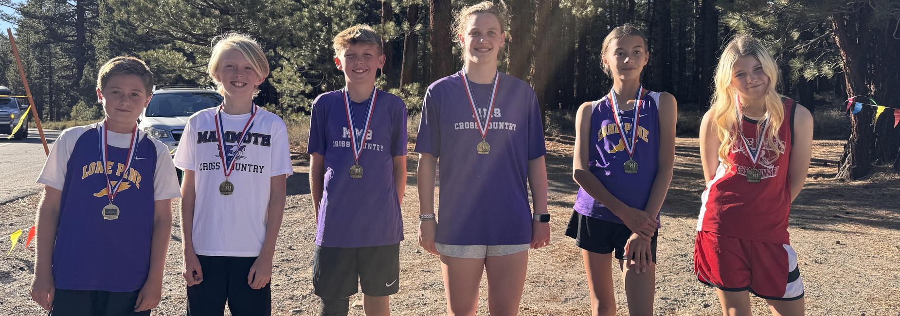 Six young athletes stand together, wearing medals and smiling after a cross country event.