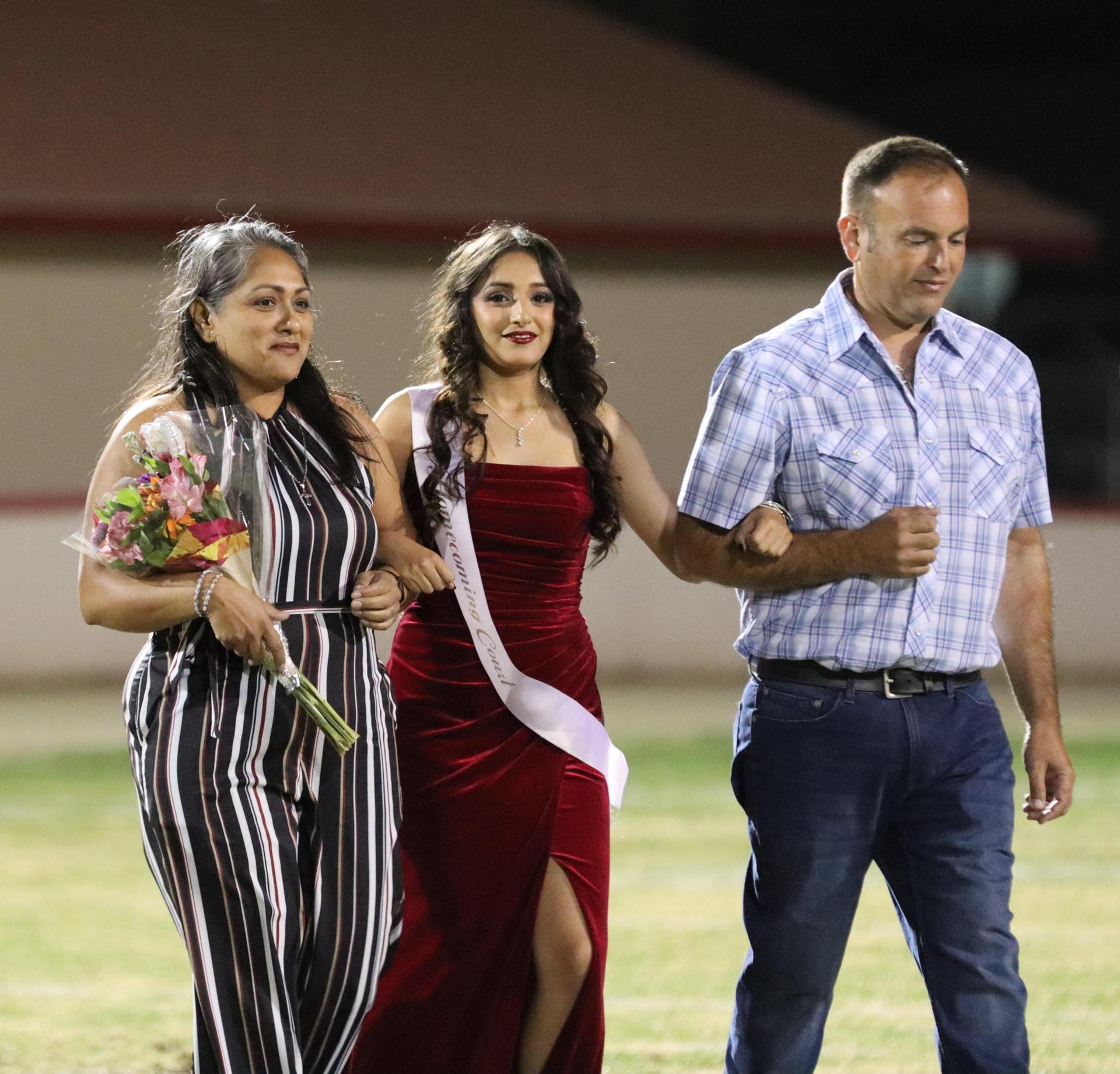 homecoming king and queen candidates walking across the field with their escorts