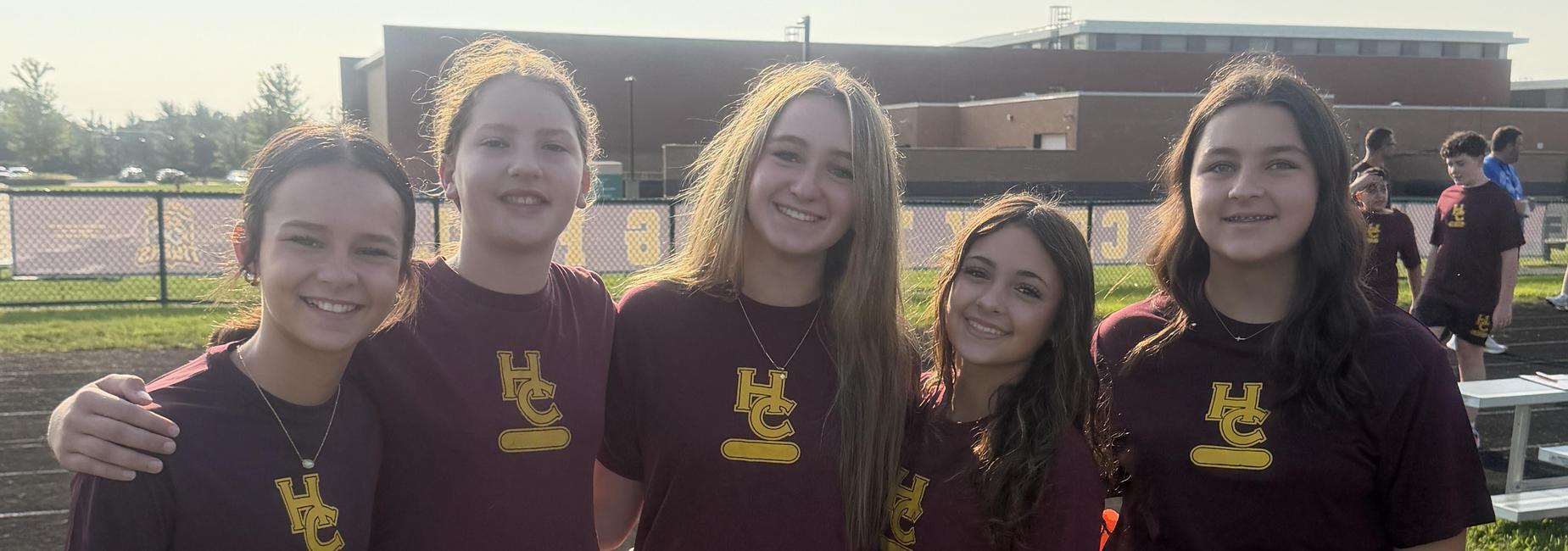 Five individuals wearing matching maroon shirts pose together outdoors.