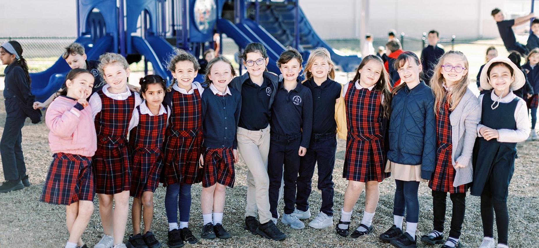 Elementary students in plaid uniforms stand together on the playground