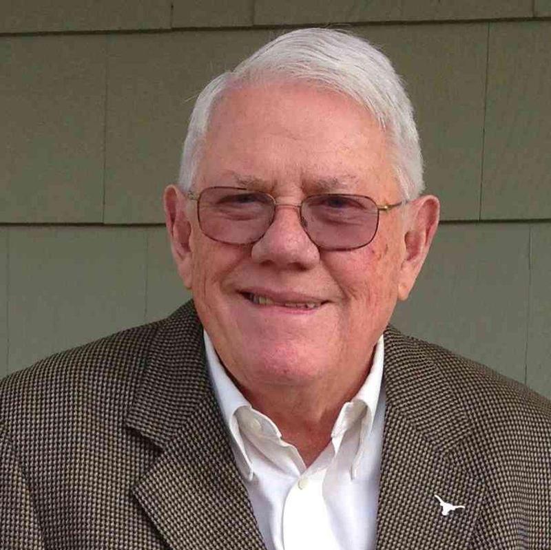 a man in a brown blazer and white hair smiles