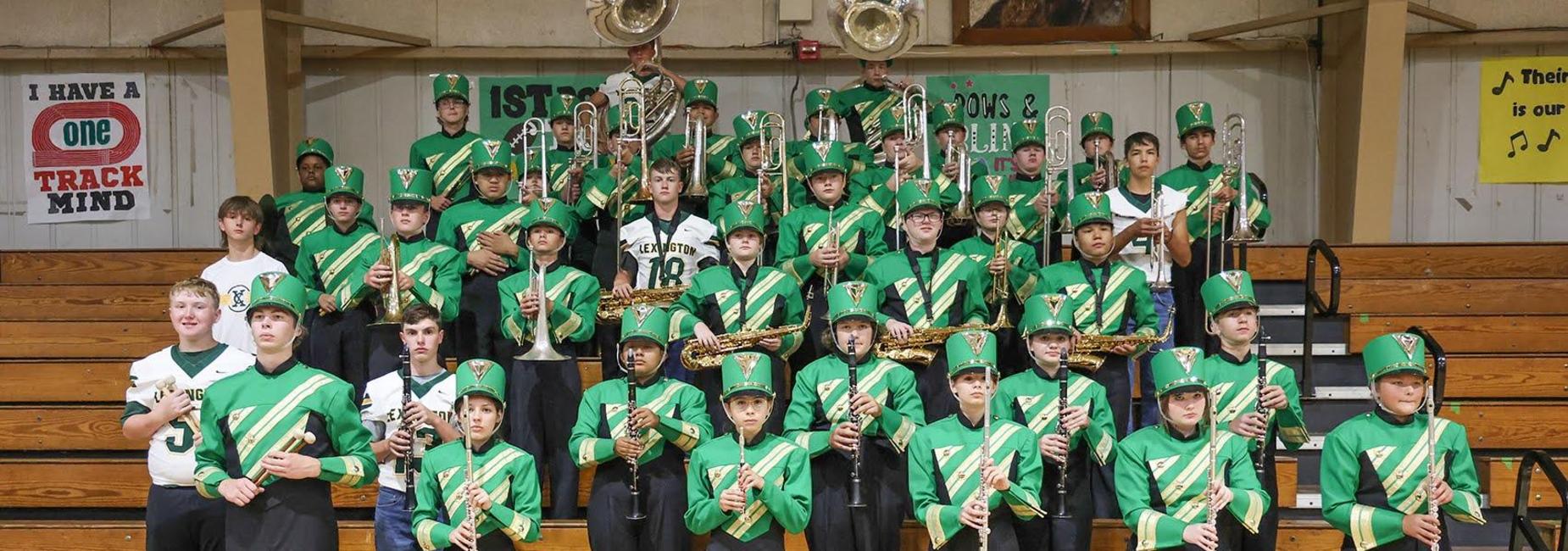Band members in uniforms posing with instruments on bleachers.