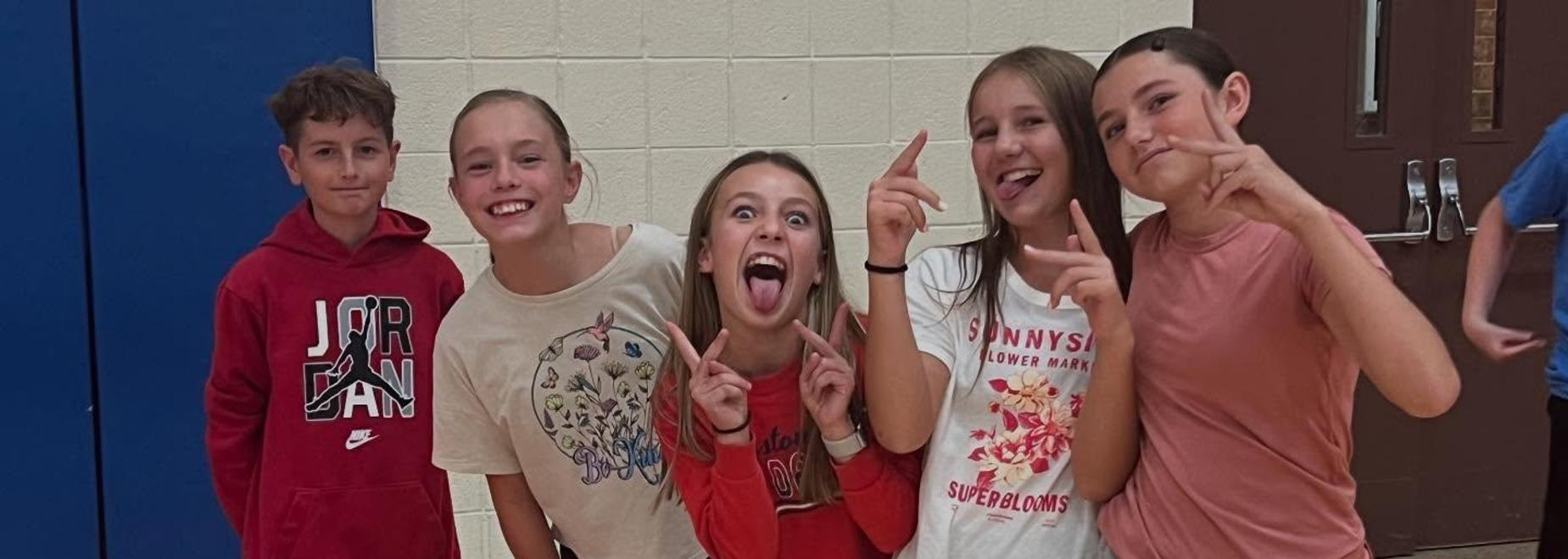 A group of five children pose for a fun photo with playful expressions.