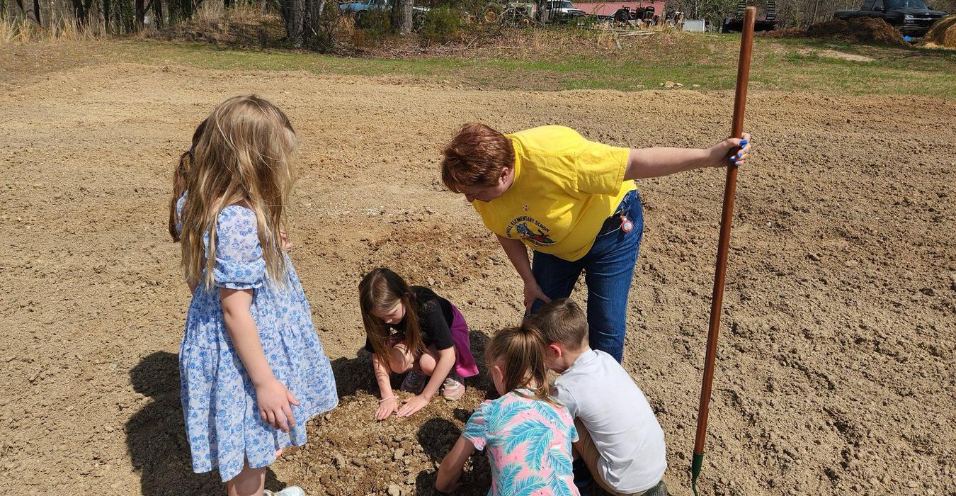 Children gather around an adult, engaging in gardening activity.