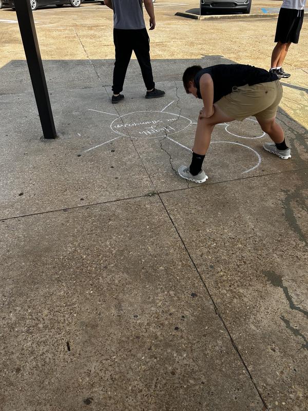 Student writing on concrete outside with yellow chalk
