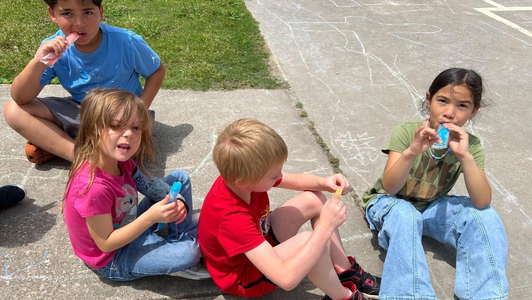Kids sitting on pavement enjoying popsicles and drawing with chalk.