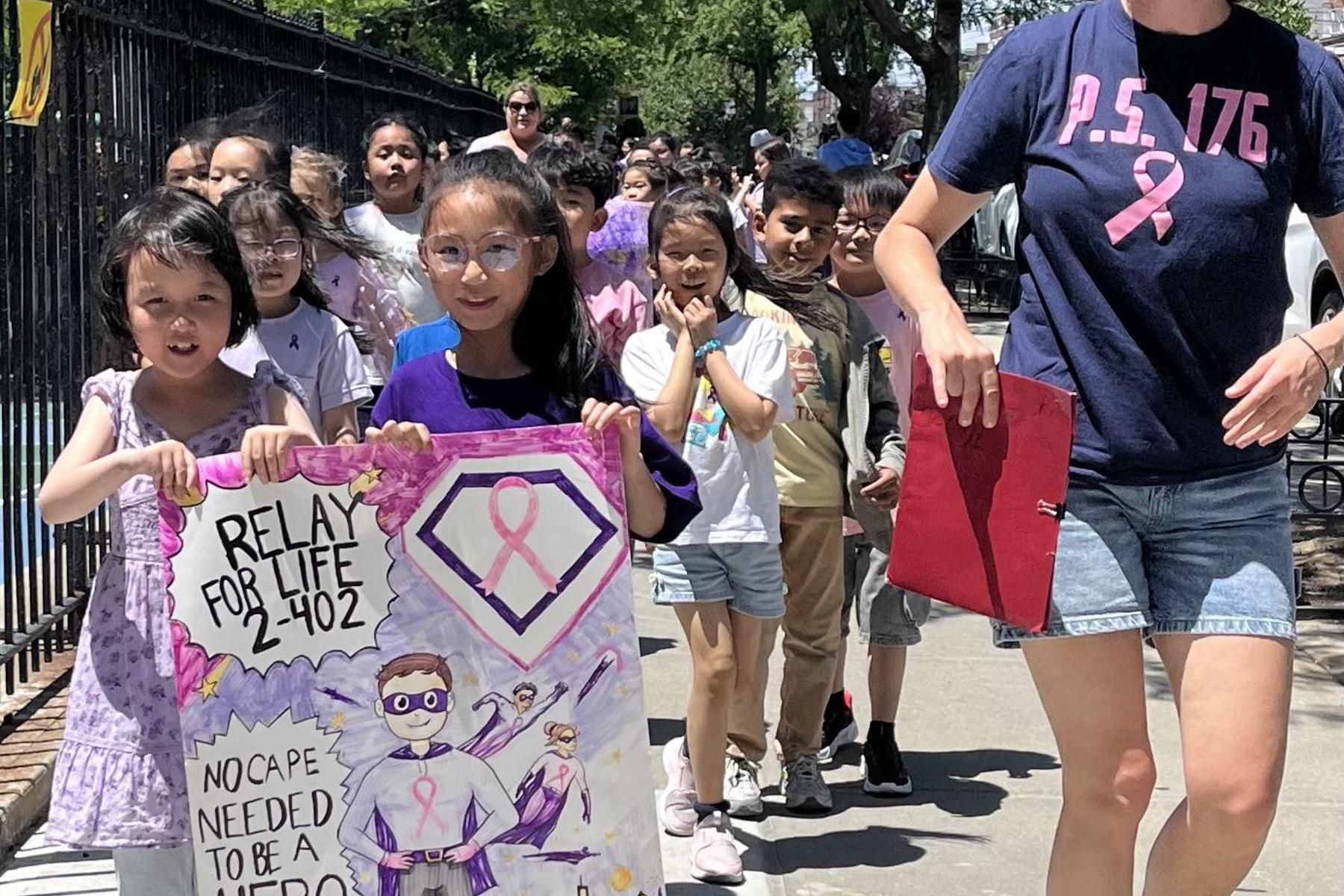 Kids walk with a vibrant Relay for Life sign showcasing a superhero theme.