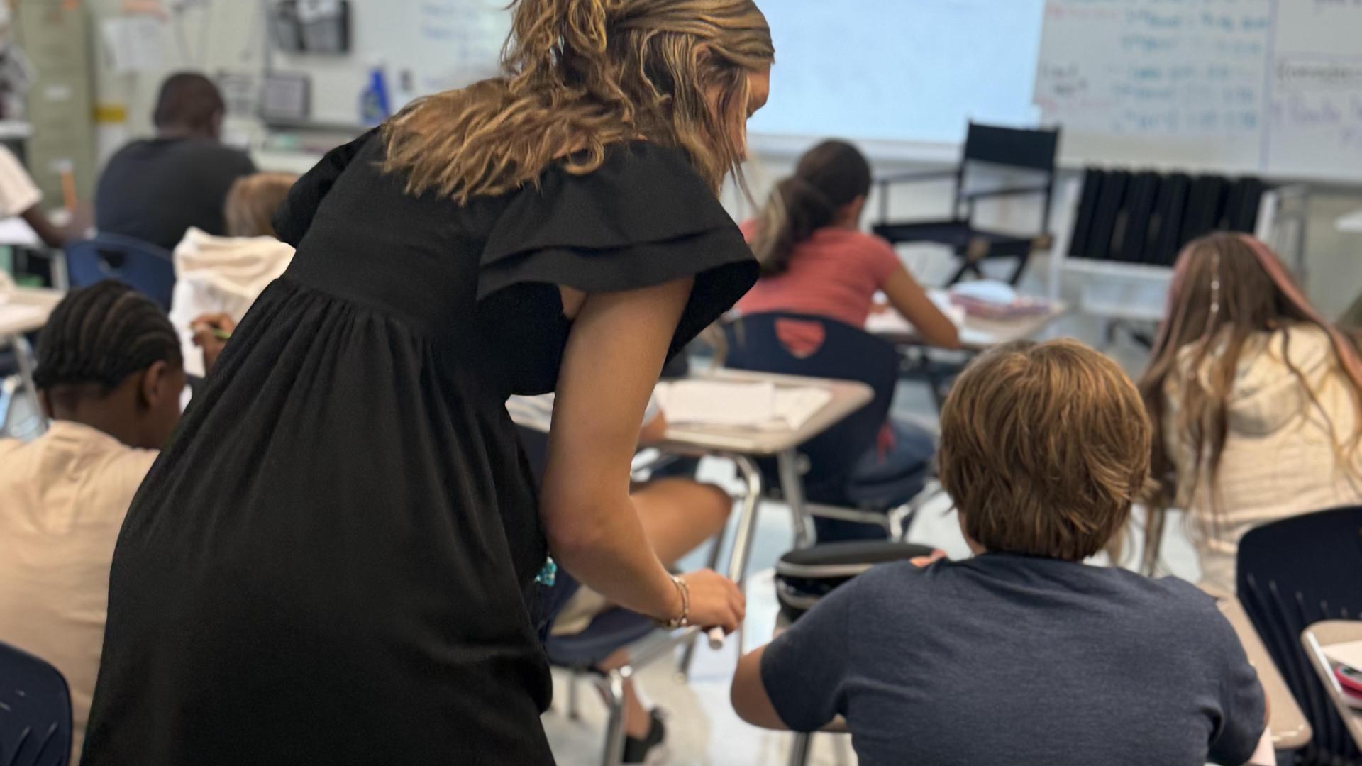 A teacher assists a student in a classroom filled with attentive students.