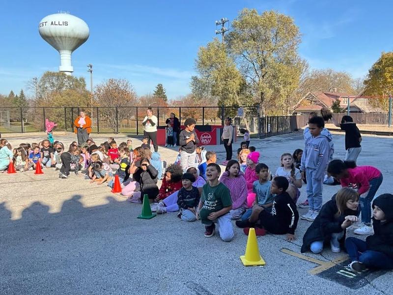 A large gathering of children outdoors near cones and a water tower during an event.