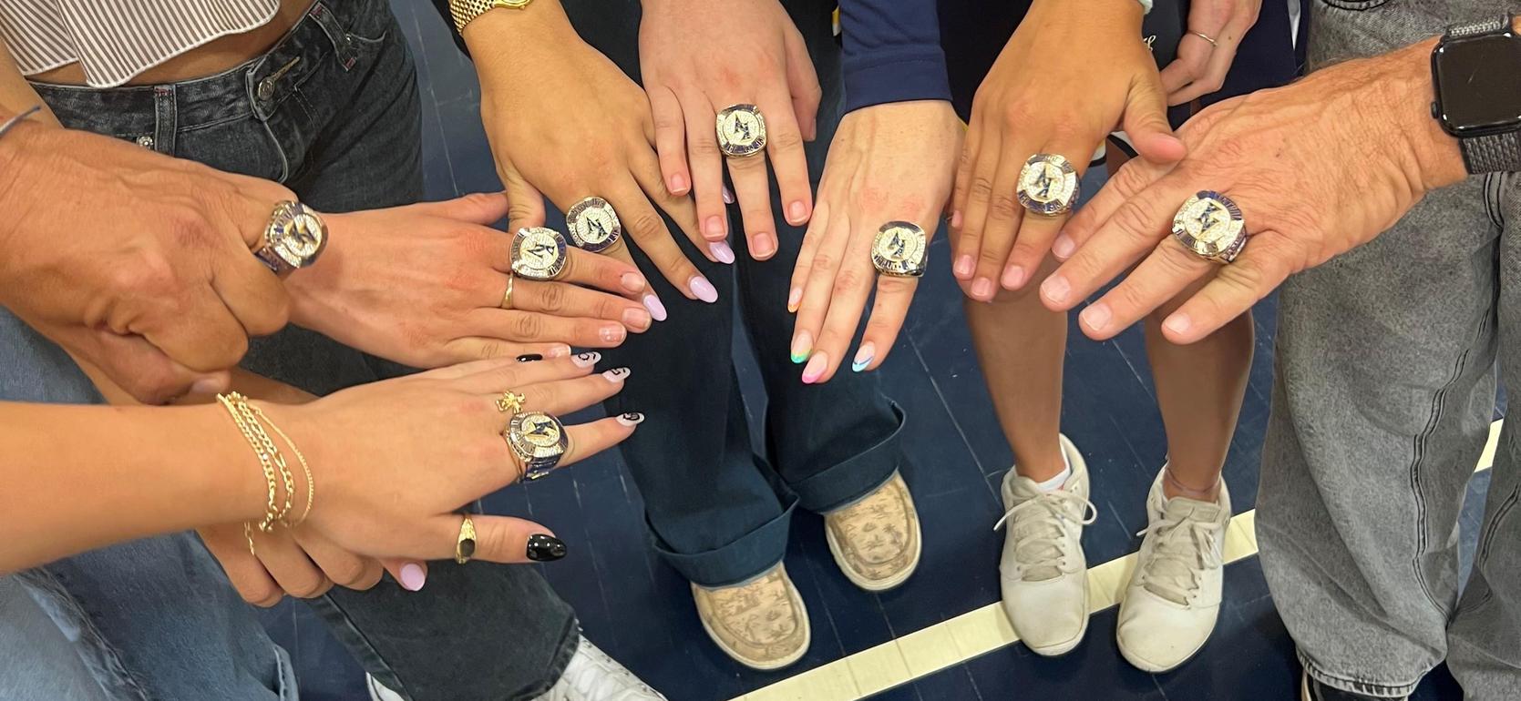 A group of hands displaying multiple championship rings, showcasing various styles and colors.