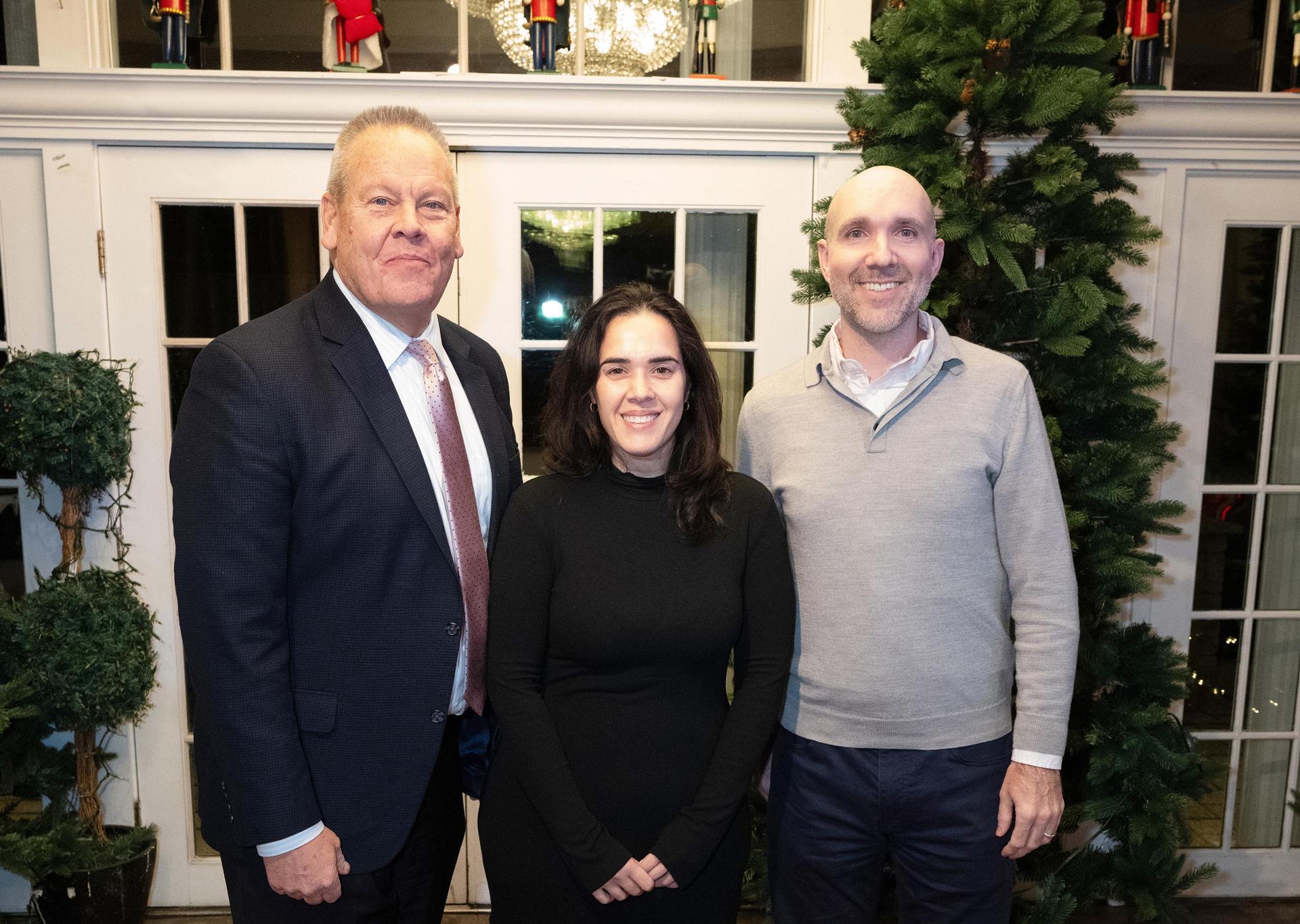 Three people standing in front of a decorated entrance with nutcracker figures and greenery.