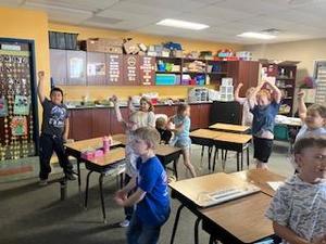 Group of kids dancing and playing in a classroom with desks.
