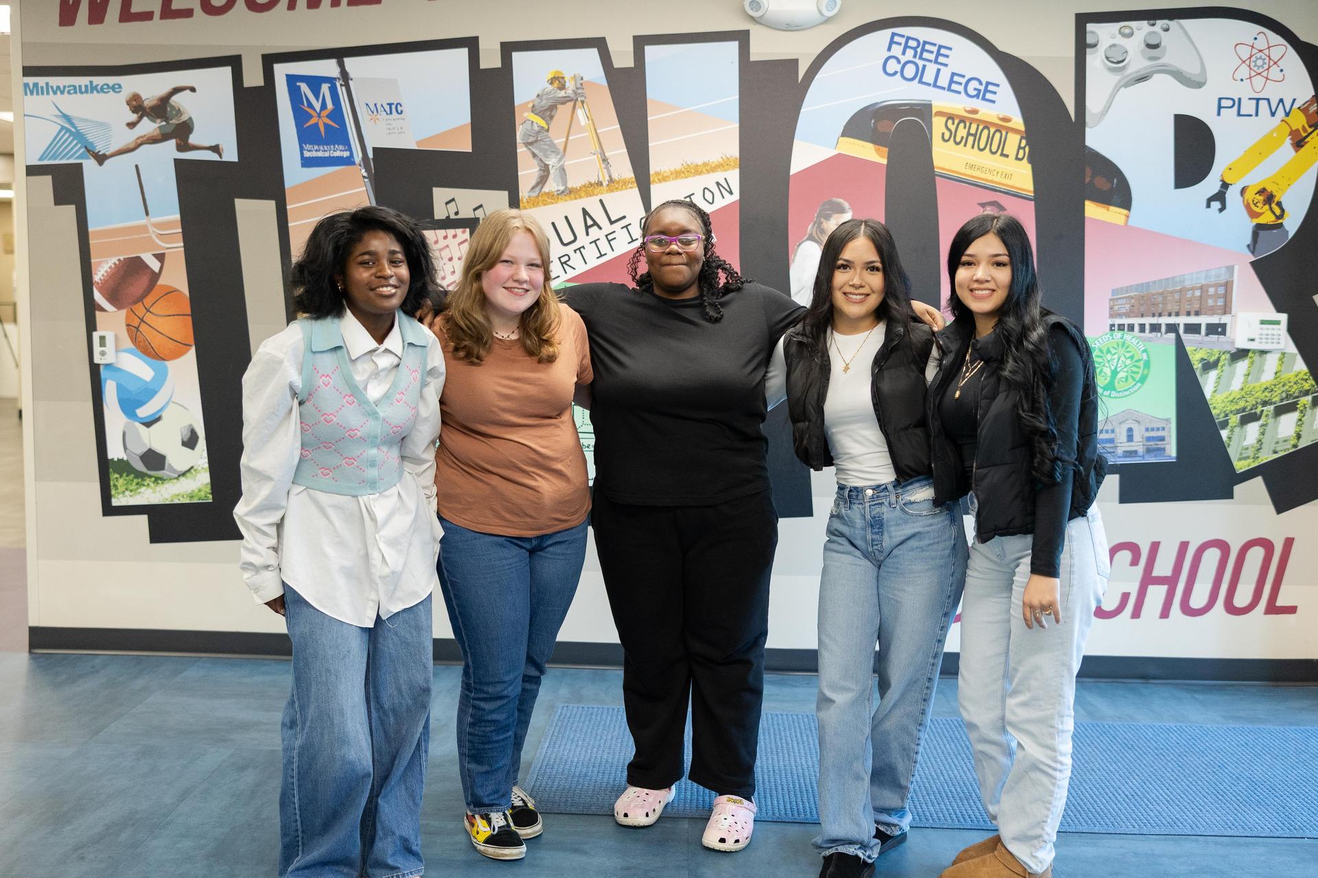 Five female Tenor students standing in front of the school mural.