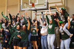 A large group of students celebrate enthusiastically in a gym, cheering and waving.