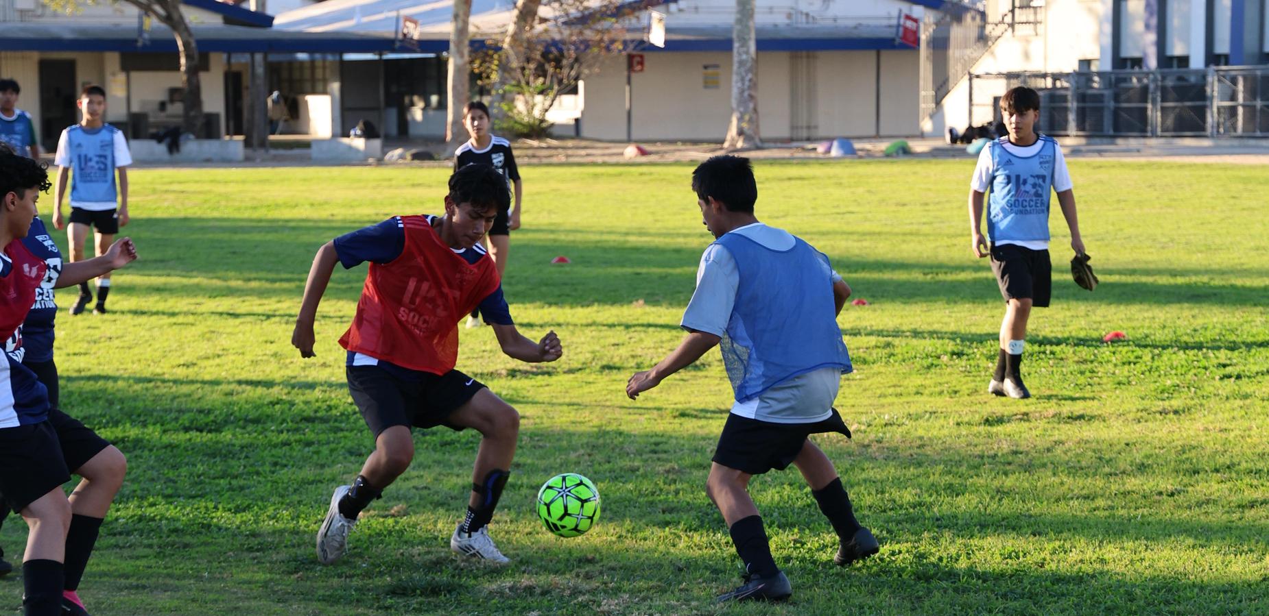 Boys playing soccer on a grassy field, dribbling a ball and wearing practice jerseys.