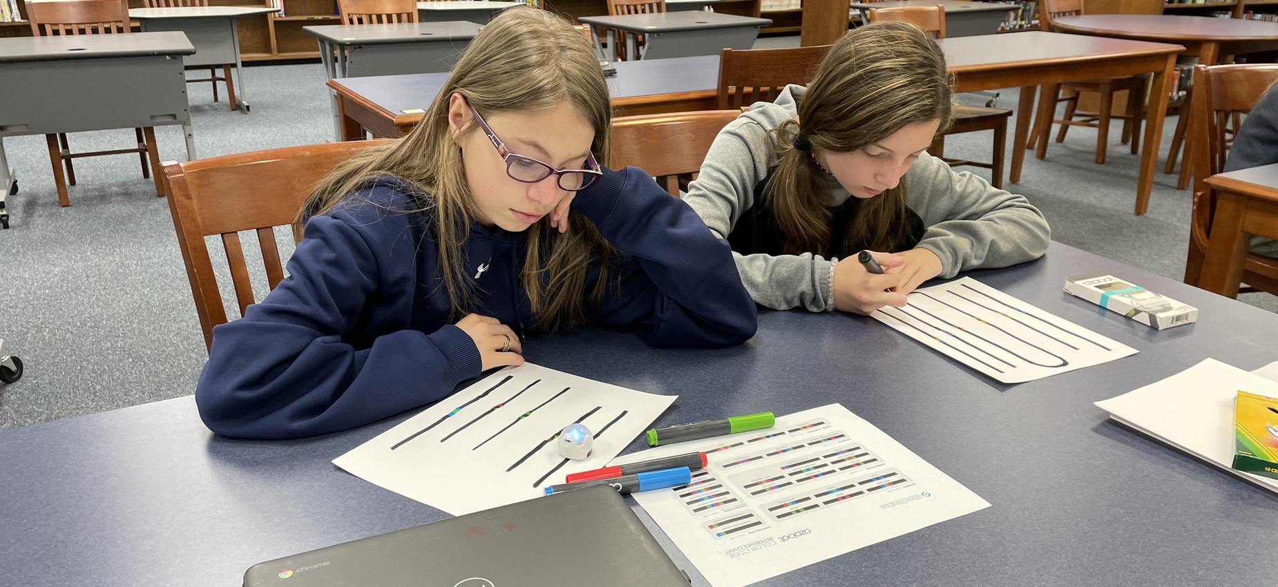 Two students write code for a robot.