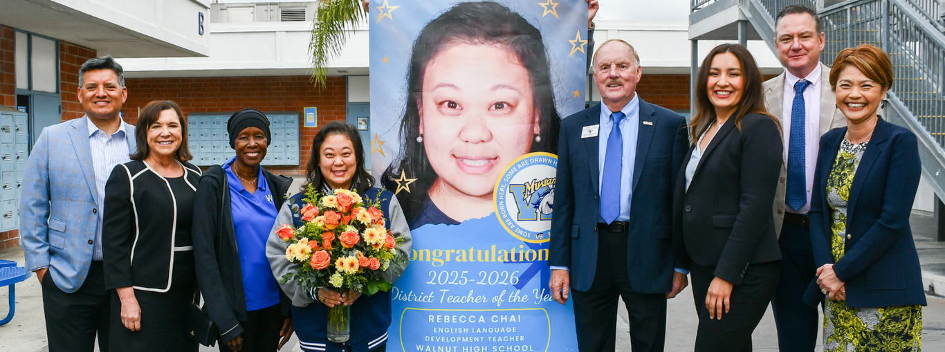 Group photo with a teacher, a large banner congratulating her, and flowers.