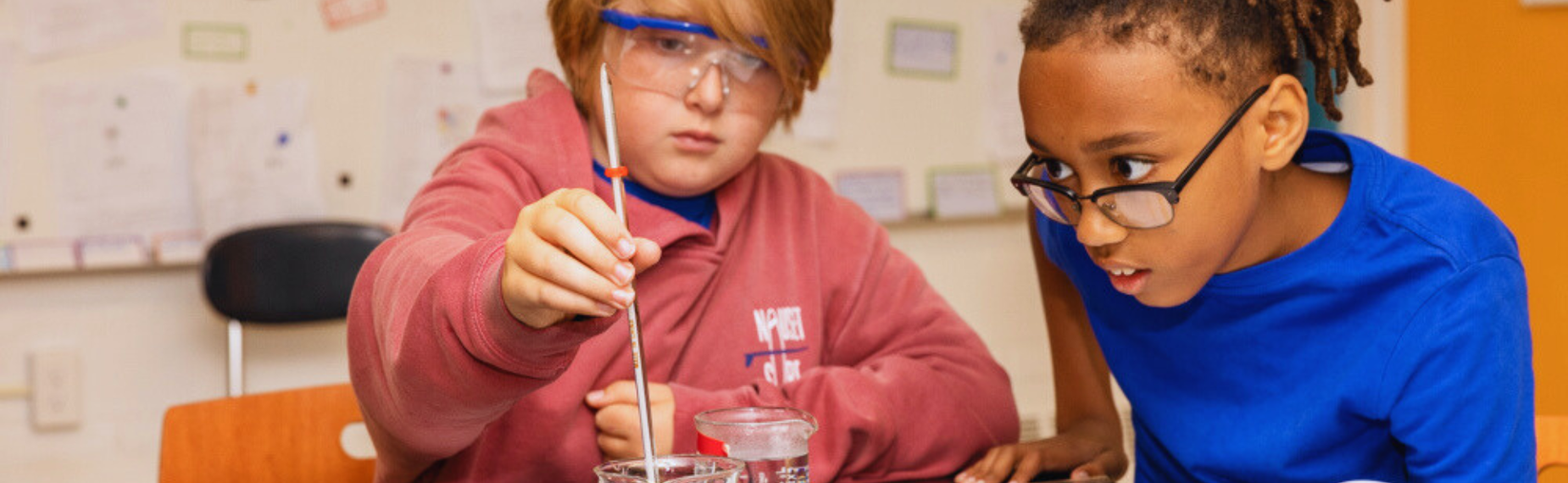 Two children experiment with liquids in a classroom setting.
