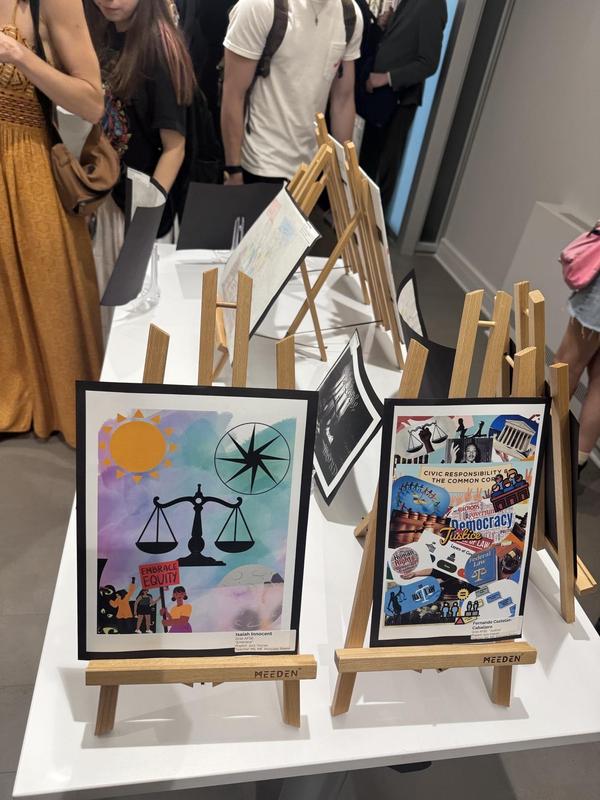 Artworks featuring scales of justice and civic themes on easels, with attendees in the background.