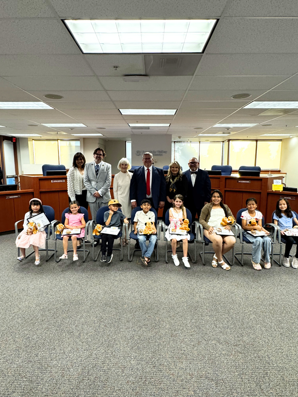 Group of adults and children posing with stuffed animals in an office setting.