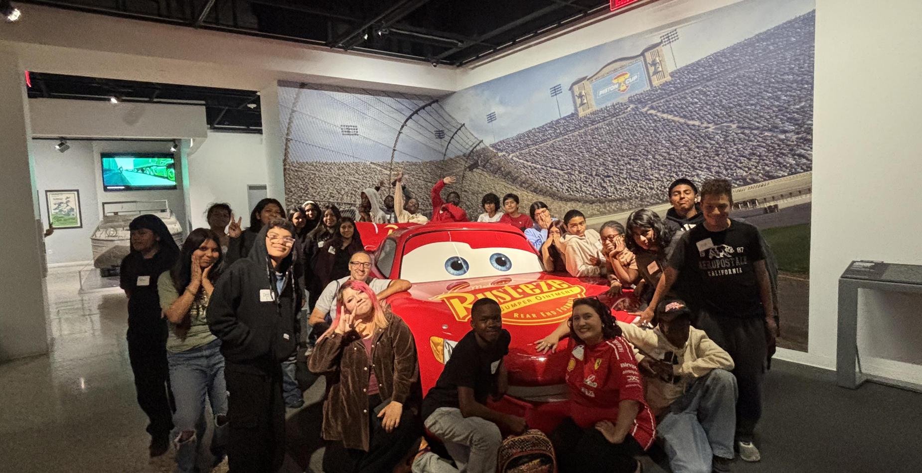 Cochran students and staff posing around a red race car at a museum field trip.