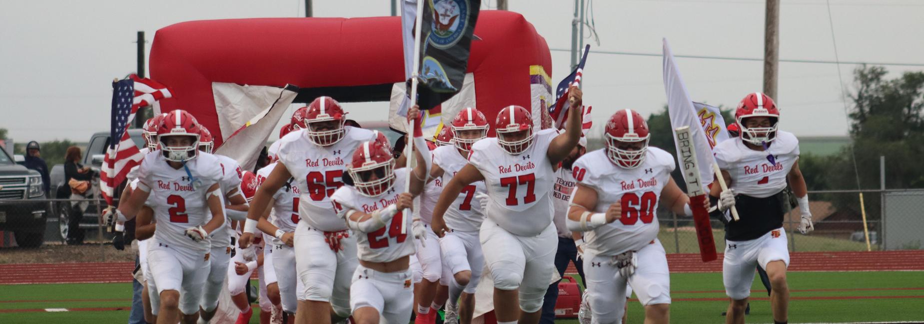 Football players running onto the field with flags before a game.