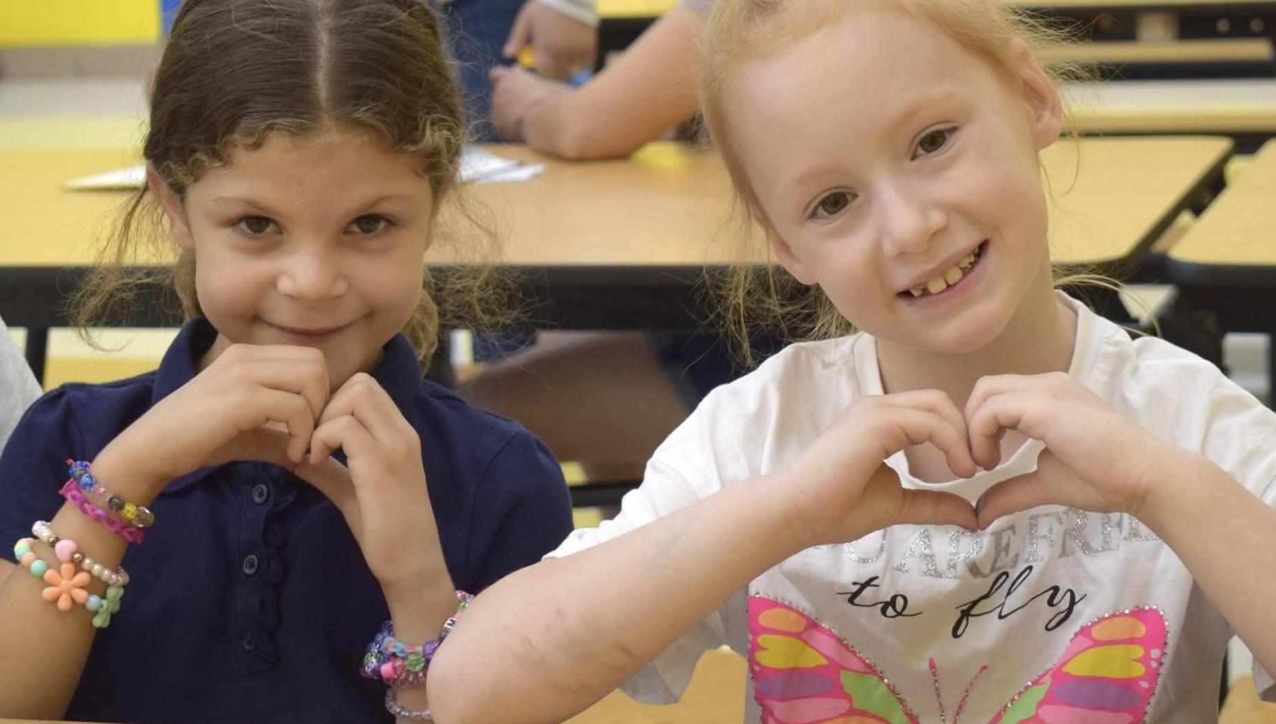 Two girls forming heart shapes with their hands, smiling at the camera.