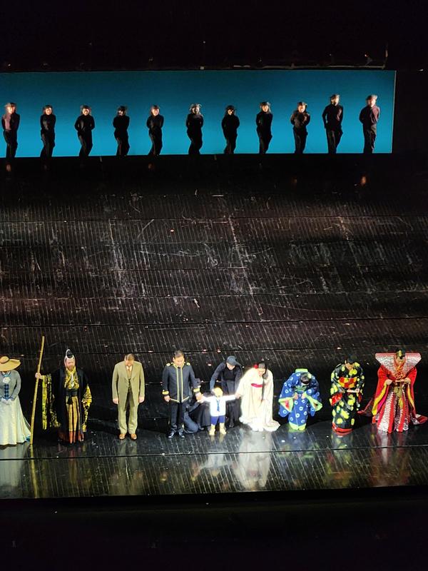 A diverse cast of performers in colorful costumes taking a bow after a show on stage.