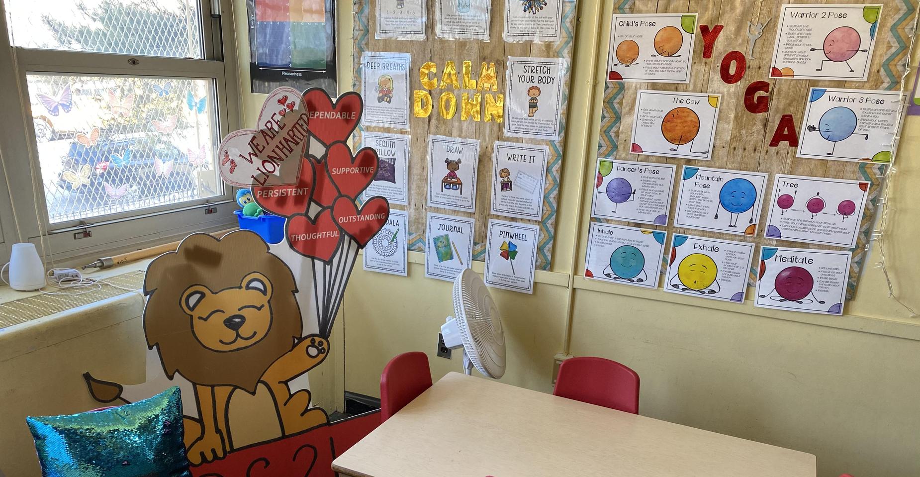 Classroom with a lion mascot holding balloons and a table with red chairs.