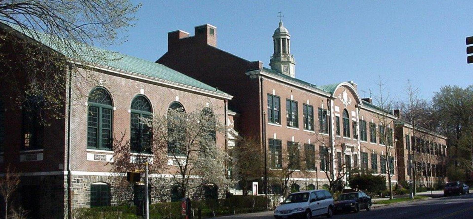 Historic school building with green windows and a cupola on a clear day.