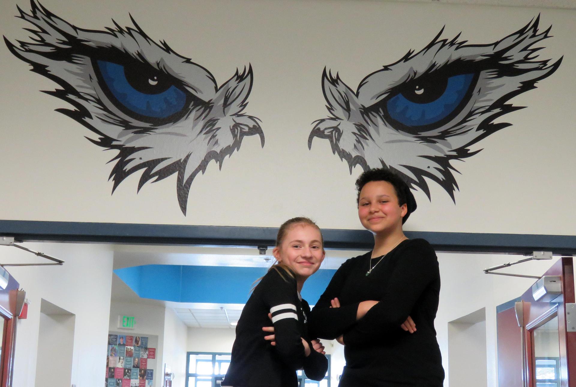Two girls pose with folded arms under the Falcon Eyes painting on the walls at Park Ridge