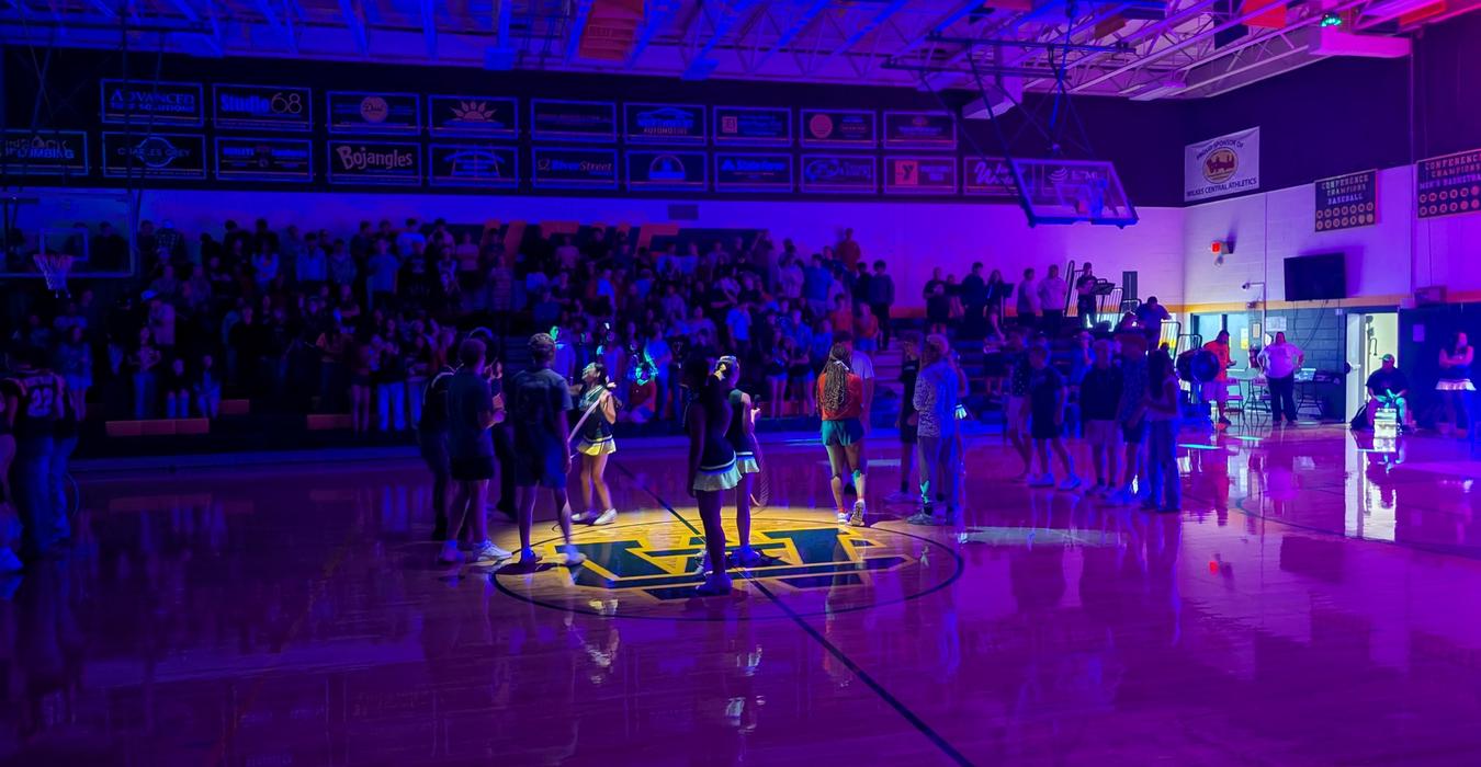 Cheerleaders and students gather under colorful lights in a gym.