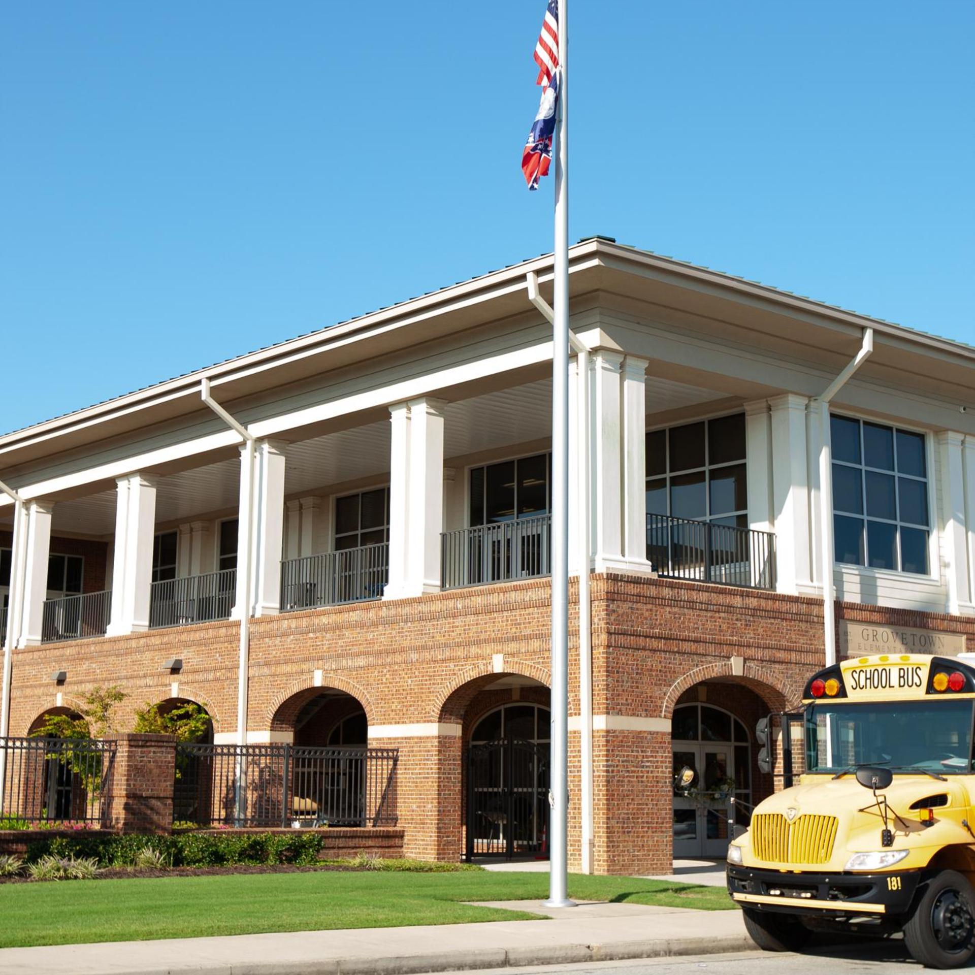A brick school building with large windows and a school bus parked in front.